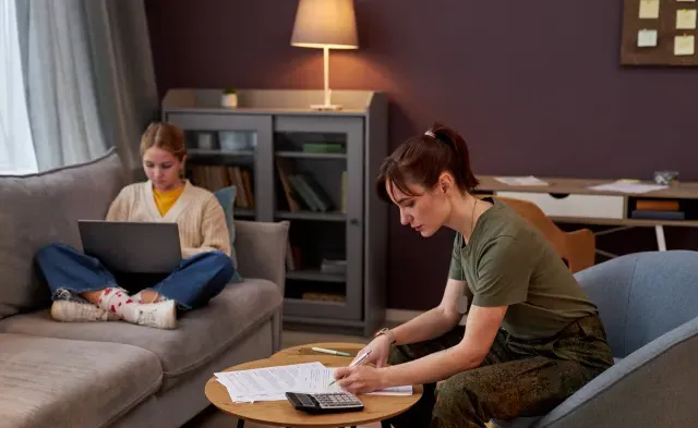 Side view portrait of young military woman working with documents at home, daughter in background, copy space